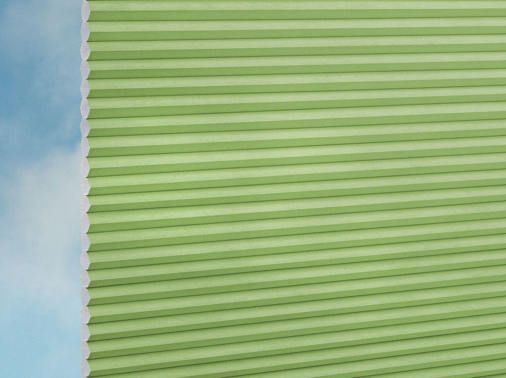 Eine Nahaufnahme der DUETTE® Fixé Unix (1.7673) Grün Jalousie von Duetteshop zeigt die horizontalen Falten mit einem blauen Himmel und weißen Wolken im Hintergrund.