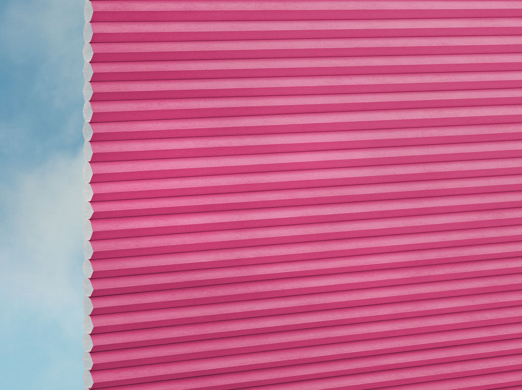 Eine Nahaufnahme von DUETTE® Fixé Unix (1.7694) Rosa Plissee nach Maß von Duetteshop, teilweise geöffnet auf der linken Seite, mit blauem Himmel und Wolken durch den Spalt.