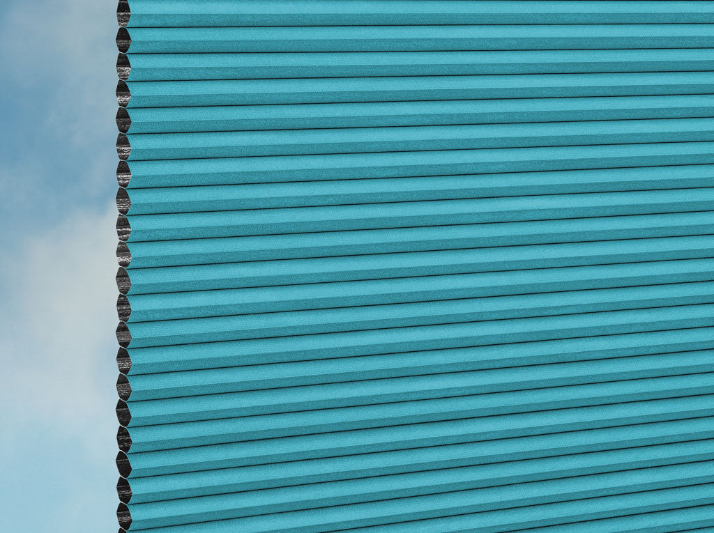 Nahaufnahme der DUETTE® Fixé Unix Dark (3.7447) Türkis-Jalousie von Duetteshop, die ihre einzigartige Struktur und Falten zeigt. Die linke Kante des maßgefertigten Rollos ist sichtbar, mit blauem Himmel und weichen Wolken im Hintergrund.