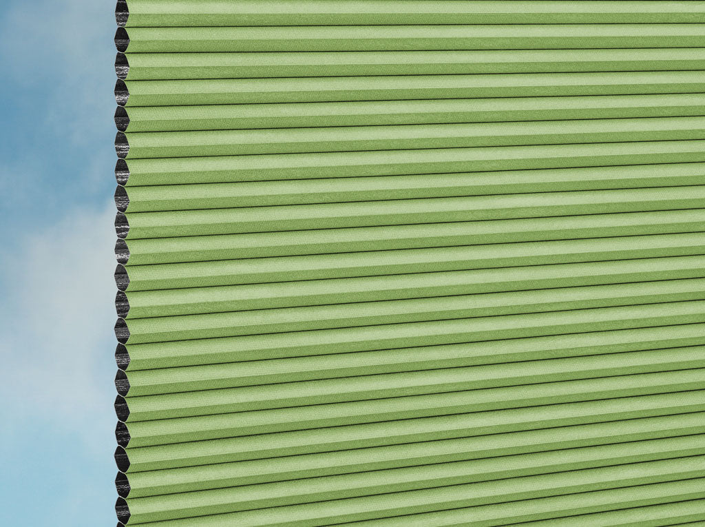 Eine Nahaufnahme des DUETTE® Fixé Unix Dark (3.7471) Grün Plissee nach Maß von Duetteshop, mit einer hellgrünen Wabenstruktur auf der rechten Seite und einem himmelblauen Hintergrund auf der linken Seite.