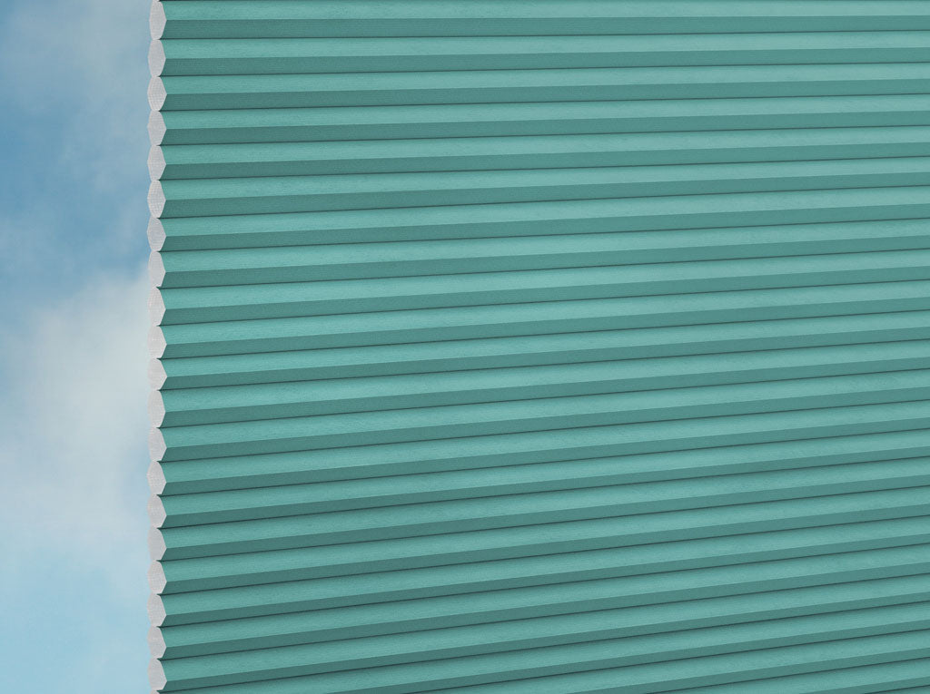 Eine Nahaufnahme von DUETTE® Fixé FR (2.7240) Türkis von Duetteshop zeigt ein tealfarbenes, horizontal plissiertes Rollo mit weichem Tageslicht und einem teilweise bewölkten Himmel, der am linken Rand sichtbar ist.