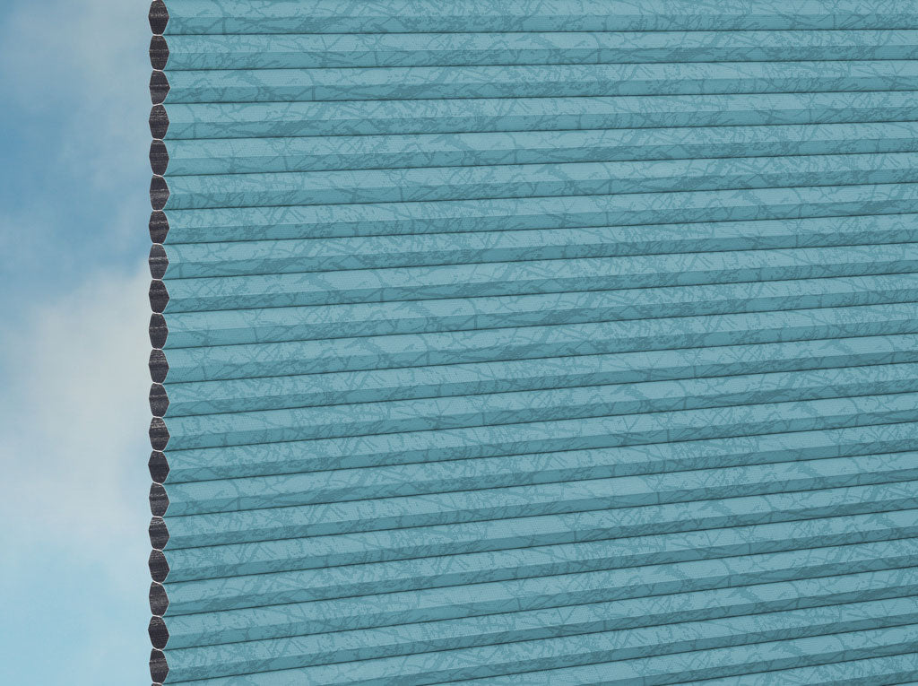 Nahaufnahme von DUETTE® Fixé Montana Dark (3.1546) Türkis von Duetteshop: Die blaue Glasfassade weist vertikale, Plissee-ähnliche Muster und Himmelsreflexe auf, mit einer sichtbaren Kante auf der linken Seite, die runde, sich wiederholende Elemente zeigt.