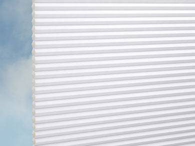 Nahaufnahme von DUETTE® Architella® Elan (3.7001) Weiß von Duetteshop, weiße Zellulose-Jalousien mit Wabenstruktur, teilweise heruntergezogen vor einem blauen Himmel mit leichten Wolken.
