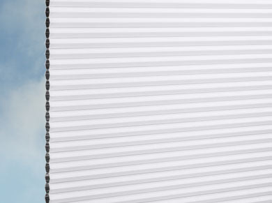 Nahaufnahme der weißen DUETTE® Architella® Elan Dark (4.6601) Weiß Wabenrollos von Duetteshop, Plissee, die ein Fenster mit blauem Himmel und leichten Wolken im Hintergrund teilweise verdecken.