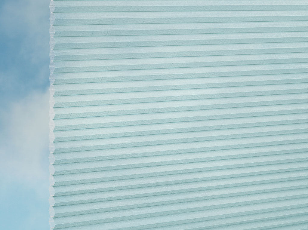 Eine Nahaufnahme von DUETTE® Fixé Batiste Sheer (4.9349) Türkis von Duetteshop in Hellblau, vor einem sanft verschwommenen, vom Himmel inspirierten Hintergrund.
