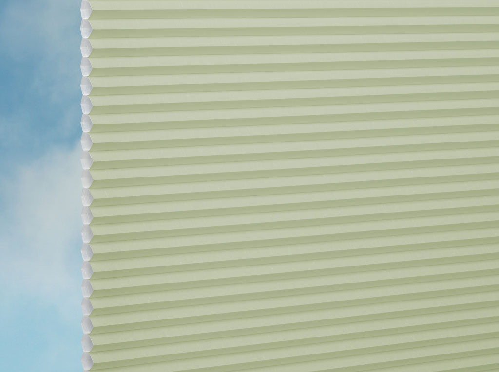 Nahaufnahme der DUETTE® Fixé Royale (4.3872) Grün Plissee nach Maß Fensterjalousien von Duetteshop mit hellgrüner Wabenstruktur vor einem blauen Himmel mit zarten weißen Wolken.